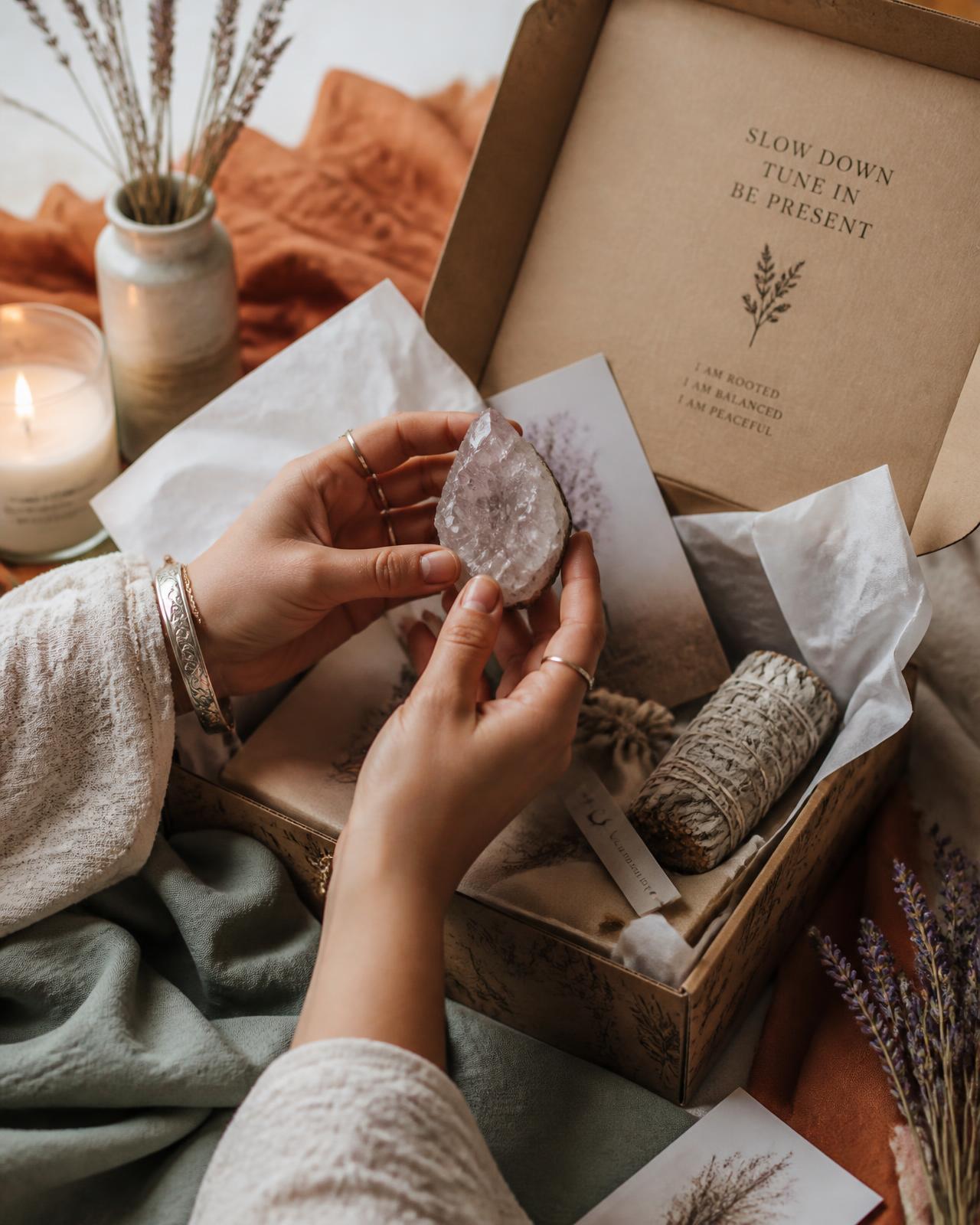 Hands lifting an amethyst geode from a Moon Box beside sage, lavender and a lit candle